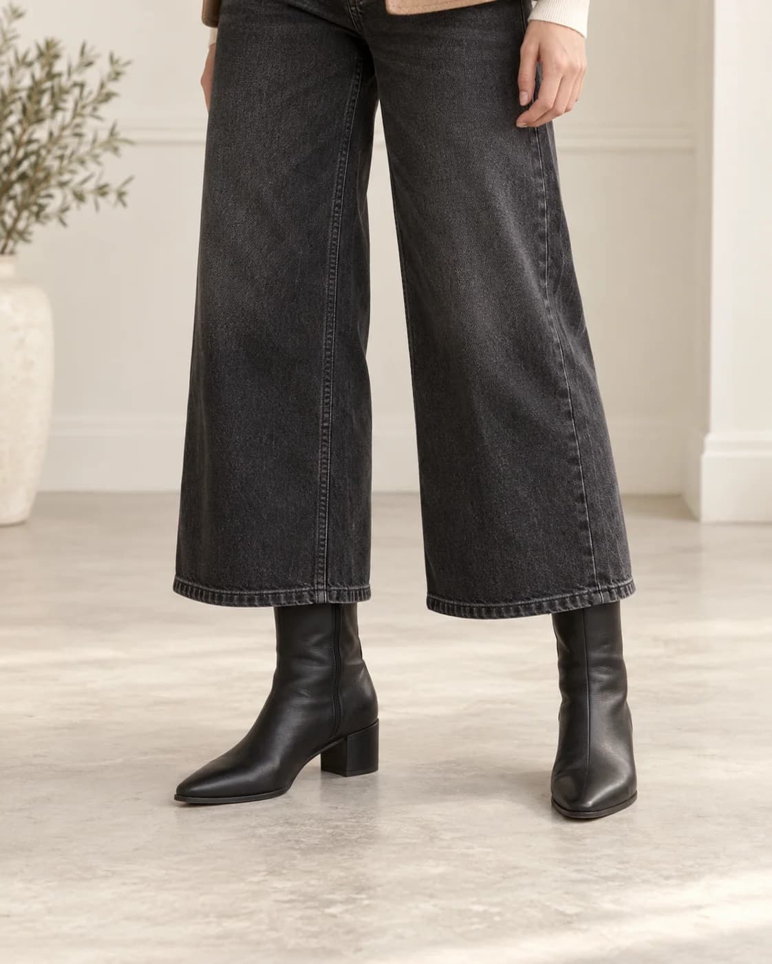 Cropped washed-black wide-leg jeans falling over slim black ankle-boot shafts, with a clear wide opening and no fabric catching at the boot tops.